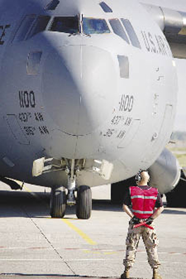 Ground crew directs military aircraft on the tarmac.