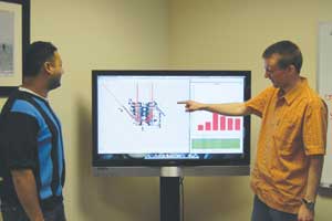 Two analysts view ground traffic patterns on a large monitor.