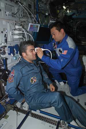 An astronaut holds an ultrasound device to another astronaut’s eye.