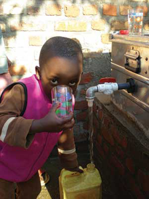 A Rwandan child drinks water from a tap and fills a jug.