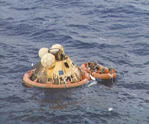 On the open sea, Apollo astronauts on a raft await pickup.