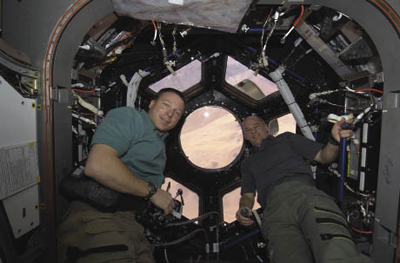 Astronauts in front of cupola windows on the International Space Station Astronauts in front of cupola windows on the International Space Station
