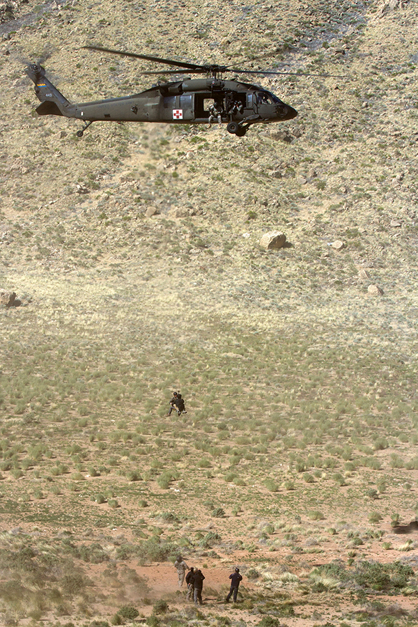 A military helicopter hovers above a group of service members