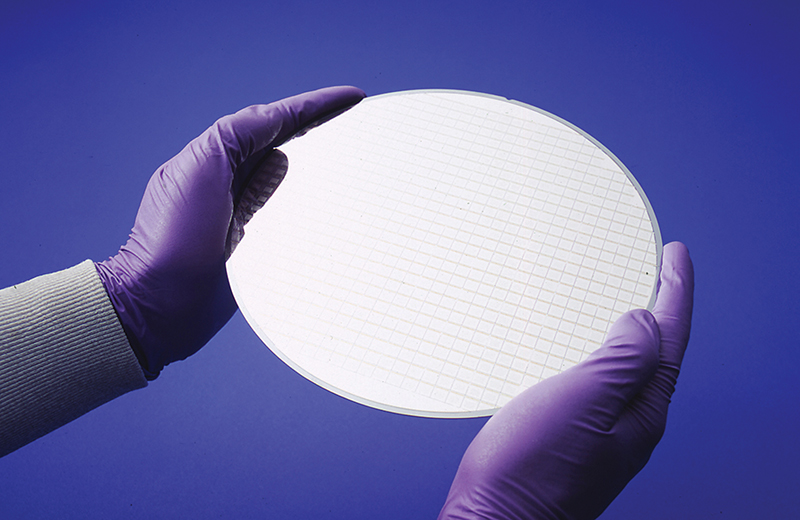 Two gloved hands hold a semiconductor wafer