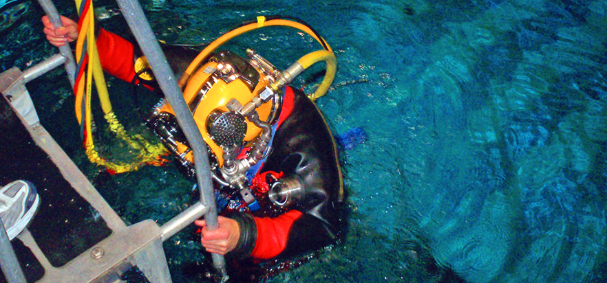 A diver wearing the Paragon suit descends a ladder into the water.