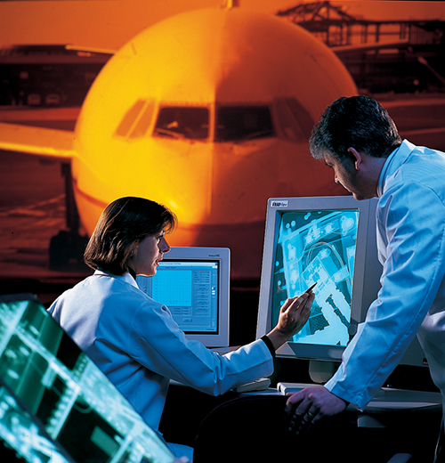 A man and a woman view radiography on computers with an image of a plane behind them