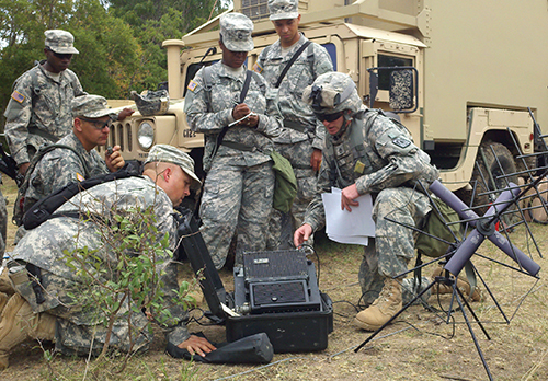 Service members in camouflage dress crowd around field communication equipment