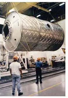 photograph of the 28 foot long, three-ton, aluminum Laboratory Module suspended from the ceiling of its construction facility before being installed on the International Space Station.