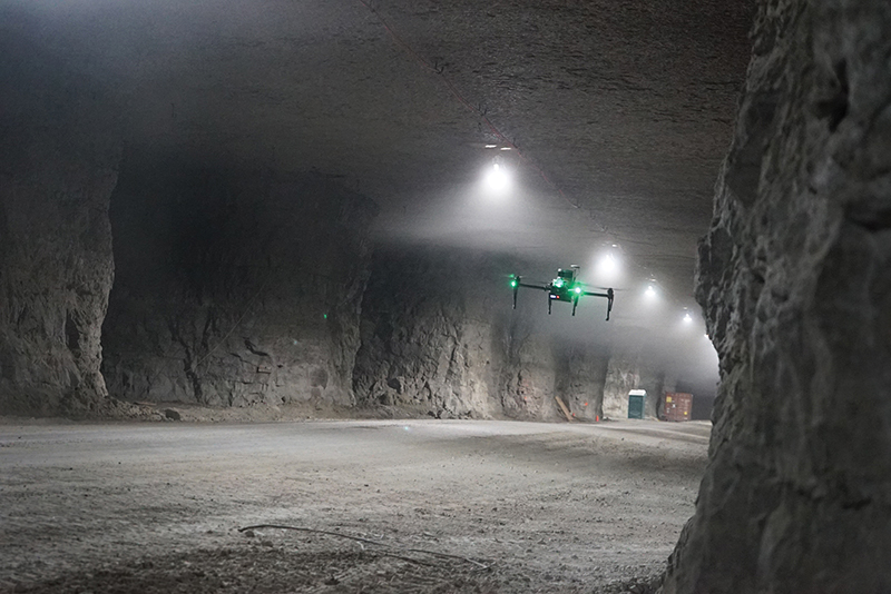 A small drone with green lights flies inside a tunnel