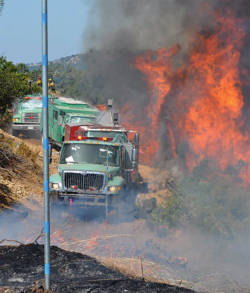 A convoy of firetrucks next to raging forest fire