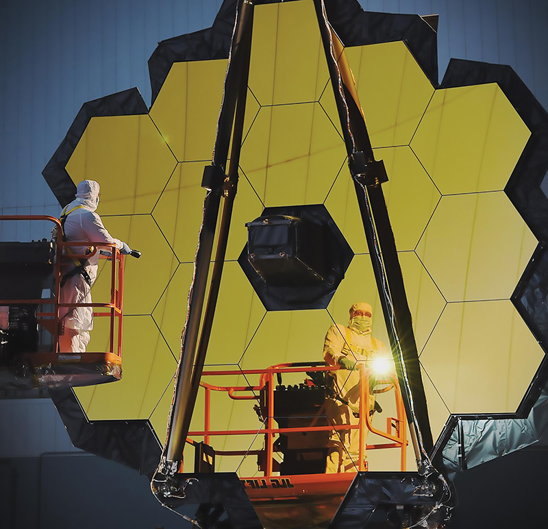 Person in cleansuit shining a flashlight into the gold-plated mirrors of the James Webb Space Telescope