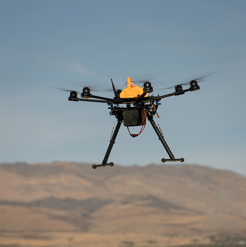 A small drone flies above desert mountains