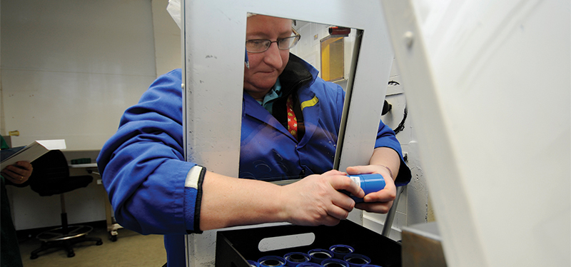 A technician packages radioactive pharmaceuticals from behind a shield