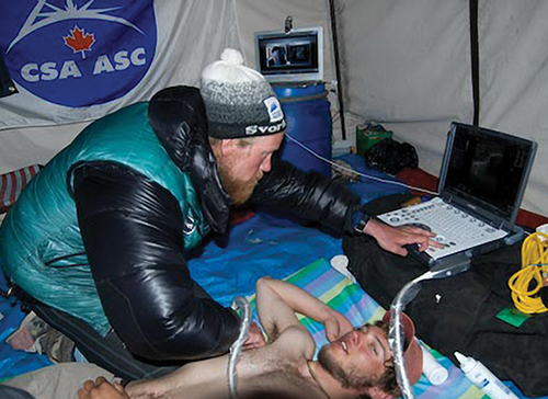 A mountain climber examines a colleague with ultrasound equipment.