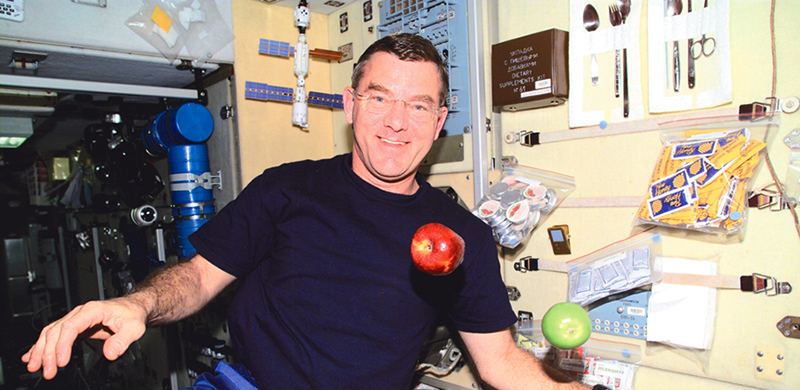 Astronaut Jim Voss on the International Space Station with a red and a green apple.