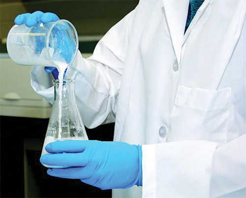 lab tech pouring clear liquid into beaker