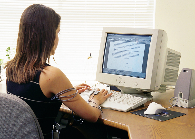 Woman typing at a computer wearing MyoMonitor