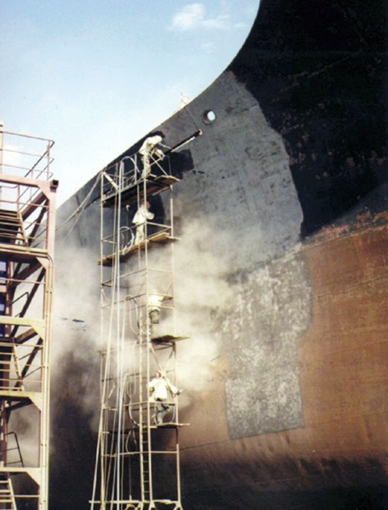 Traditional grit blasting being done to a ship by workers on a scaffold