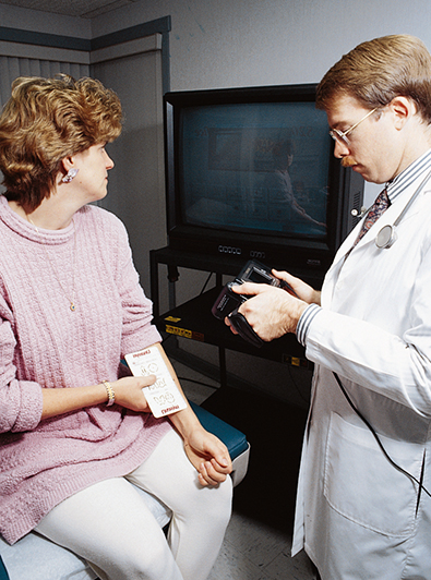 physician inspects a mole on patient's arm with a novel computerized microcomputer