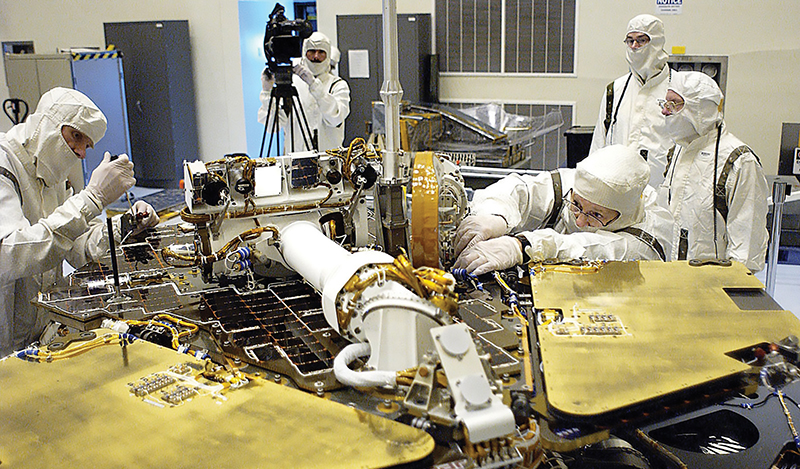 Technicians in clean room gear remove a circuit board from the Mars Exploration Rover 2