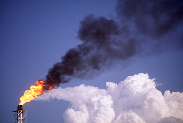 Flare stack with white cloud in background at oil refinery