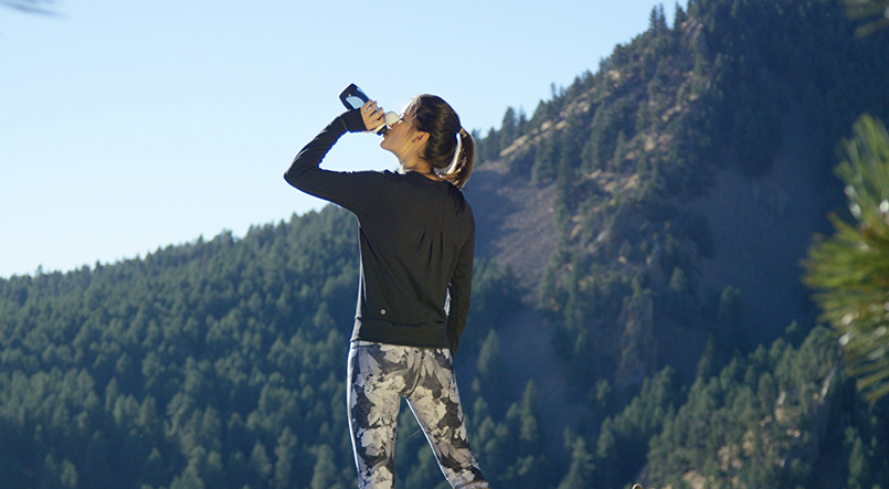A woman on a mountain drinks from a Pod+ water bottle