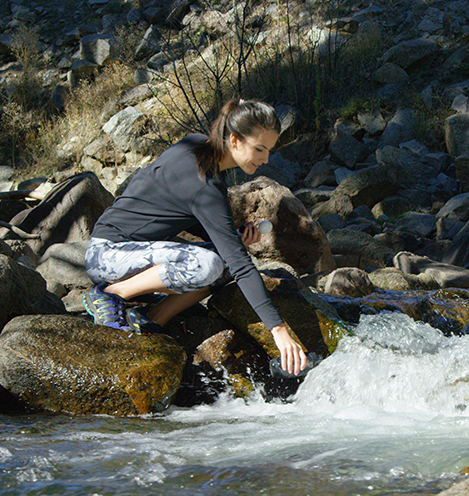 A woman fills a Pod+ water bottle from a flowing stream