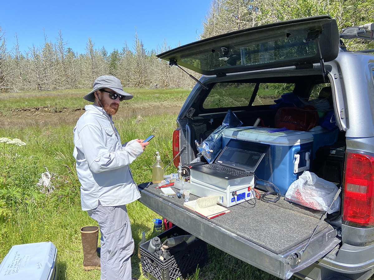 Nicholas Ward, a researcher with the Department of Energy’s Pacific Northwest National Laboratory, uses an OKSI-developed capillary absorption spectrometer for field measurements of methane in coastal wetlands of Washington state in June of 2021