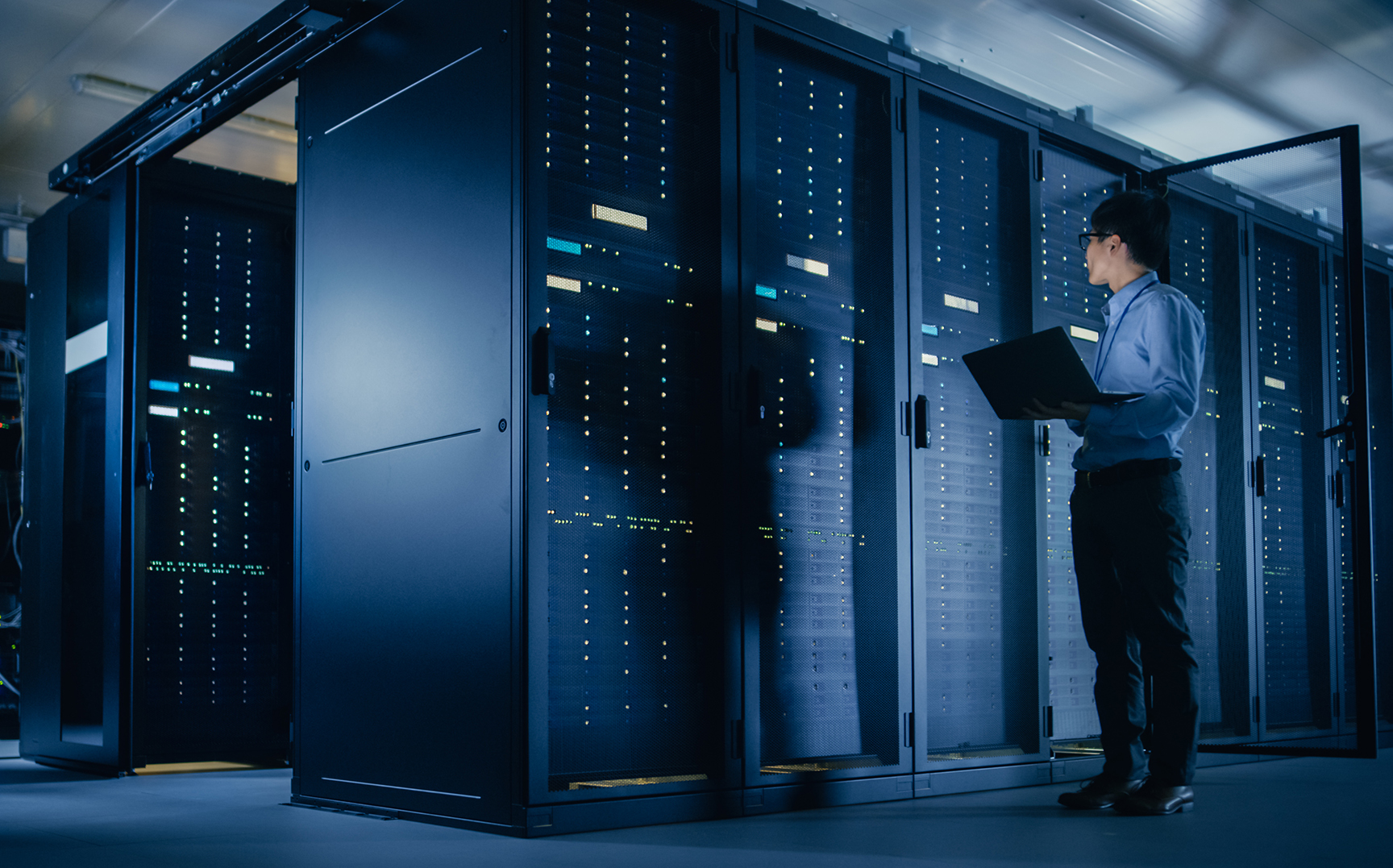 A man holds a laptop in a data center filled with stacks of server equipment