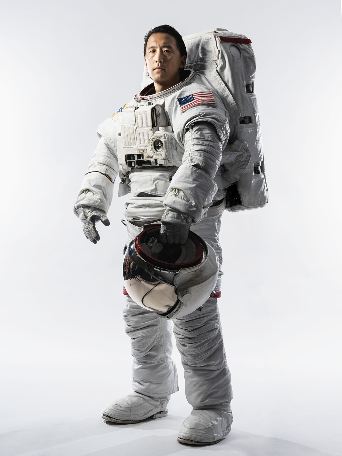 Astronaut poses in spacesuit with helmet in hand