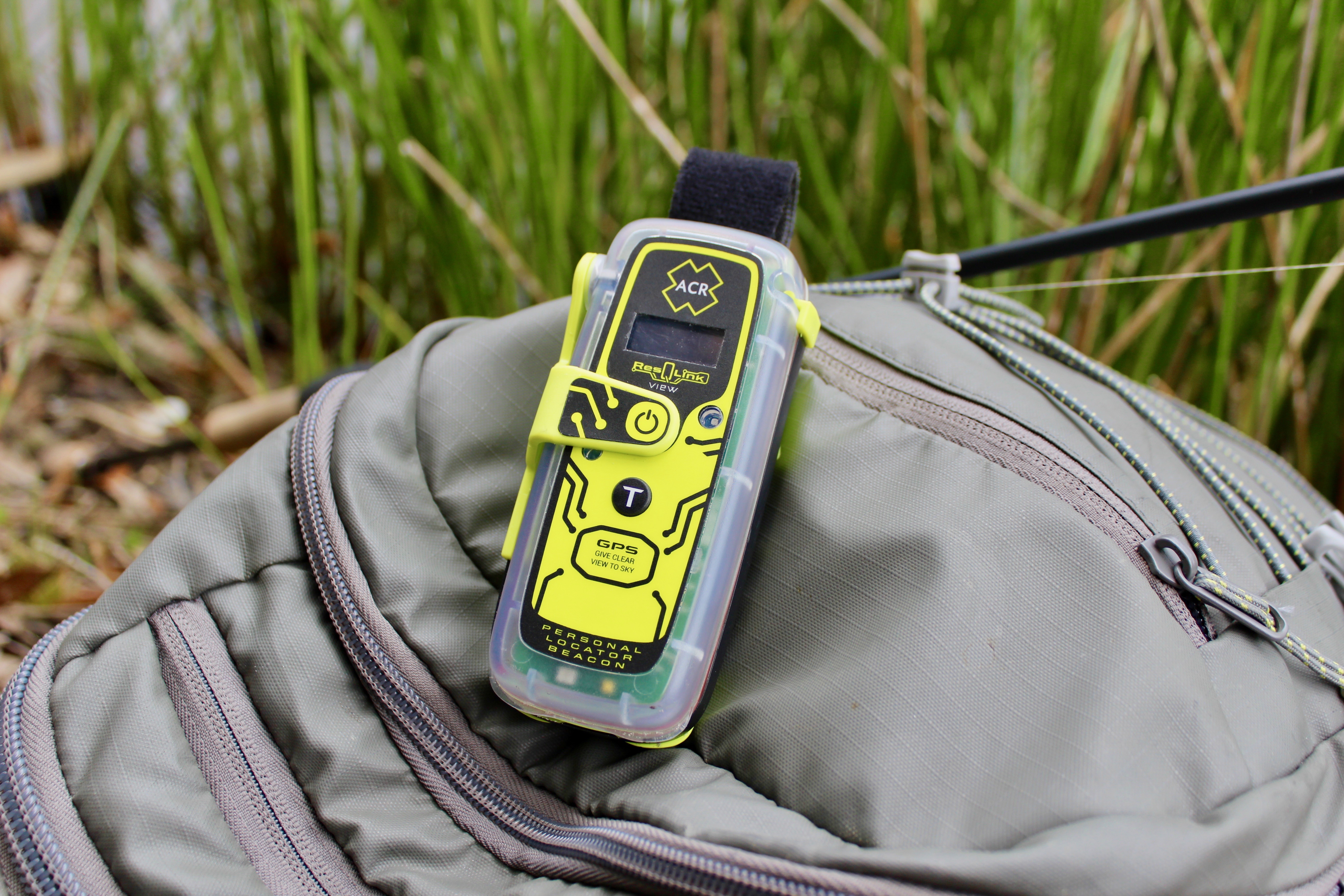 A neon yellow and black ResQLink device laying on a beige bag in an outdoor setting with tall grasses blurred in the background.