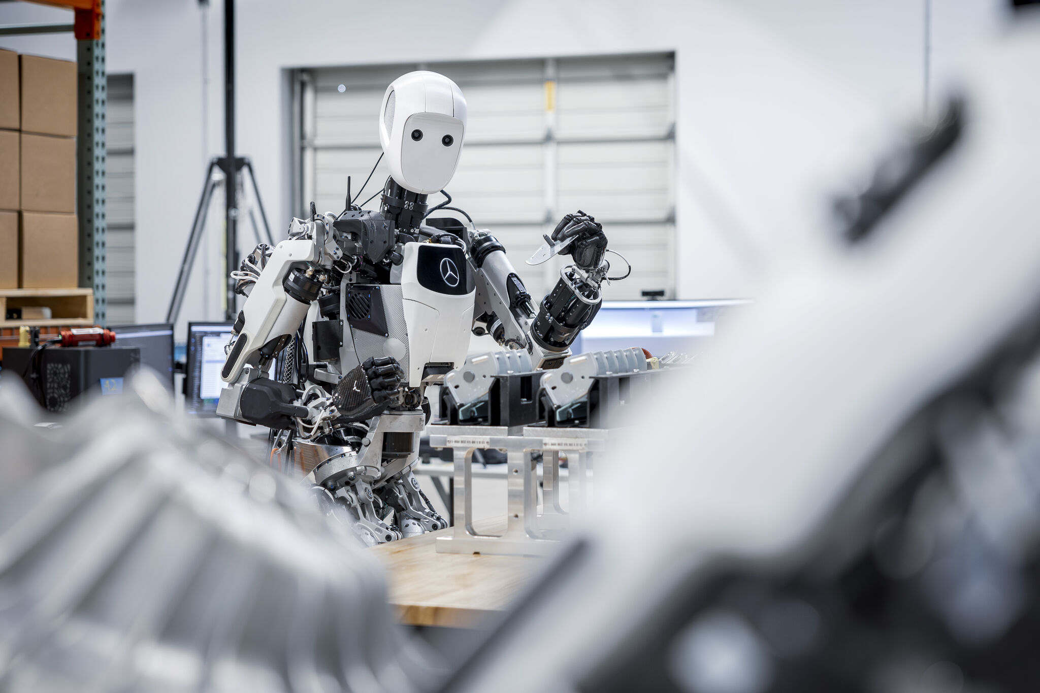 A white and black, humanoid robot holds a blade or machine part in a factory setting. 