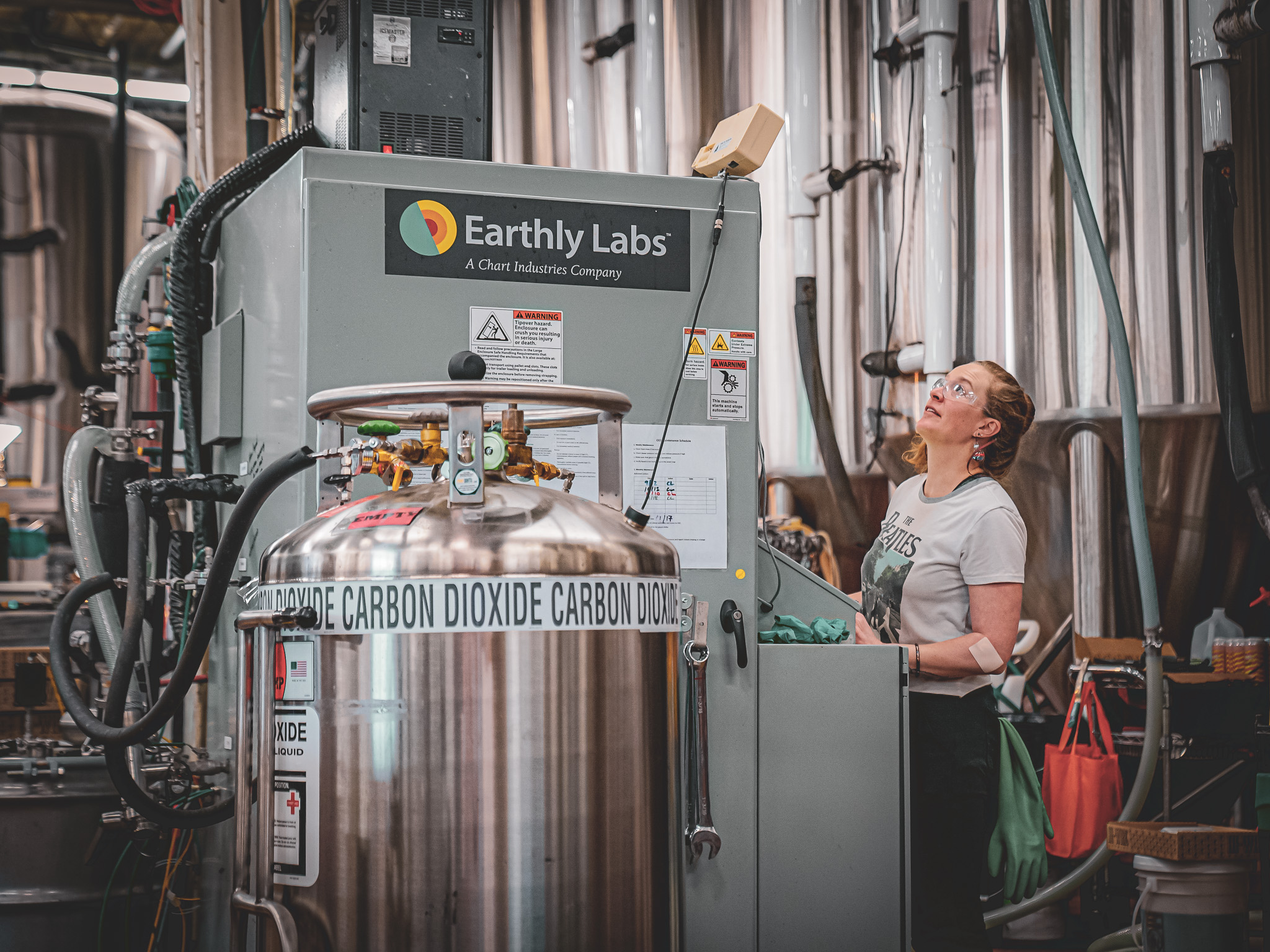 A woman controls an Earthly Labs-branded machine in a factory setting; a tank that says “carbon dioxide” is in the foreground. 