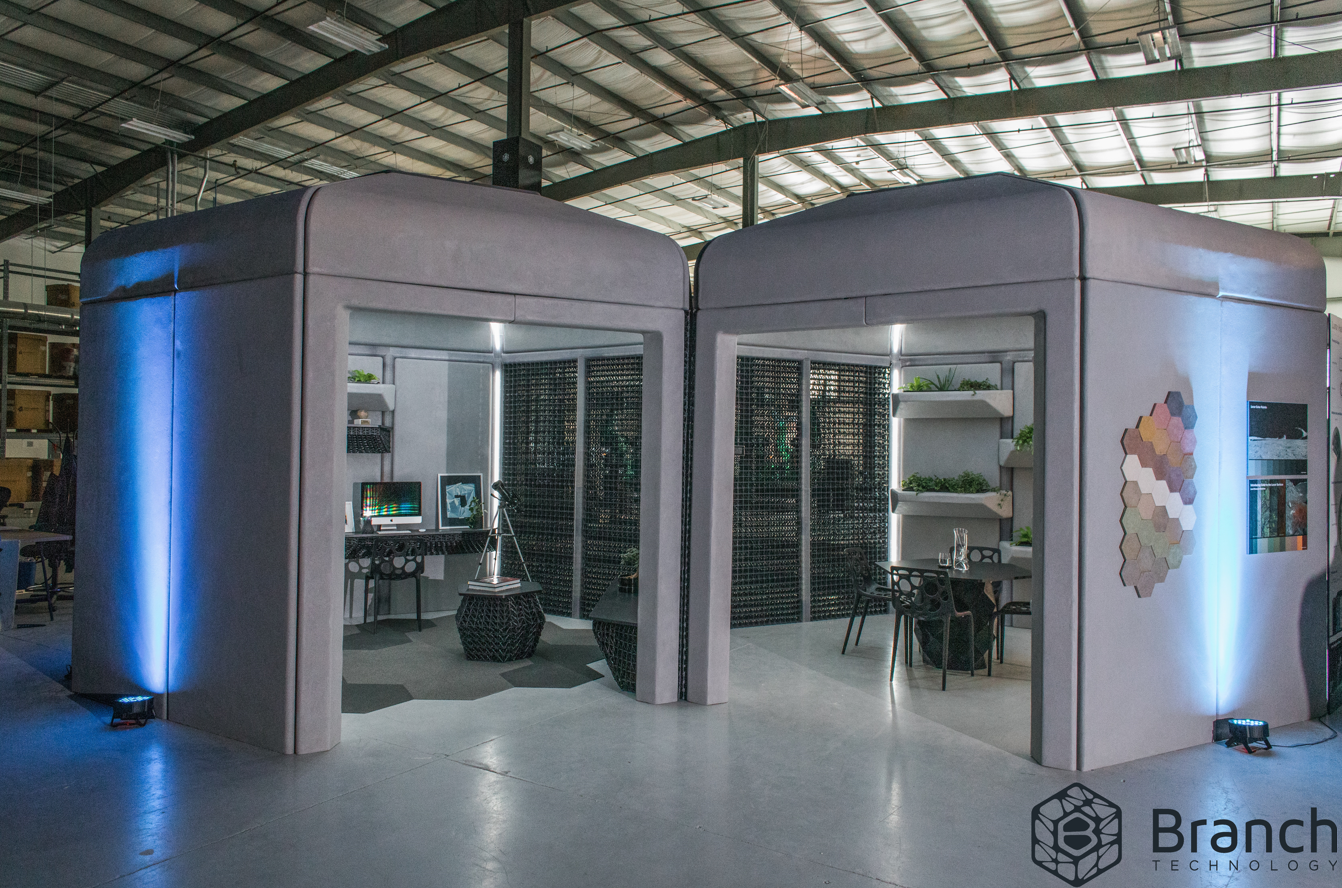 Two boxy structures, one with an office-like interior and the other with an eating area, side-by-side in a hangar-like location. 