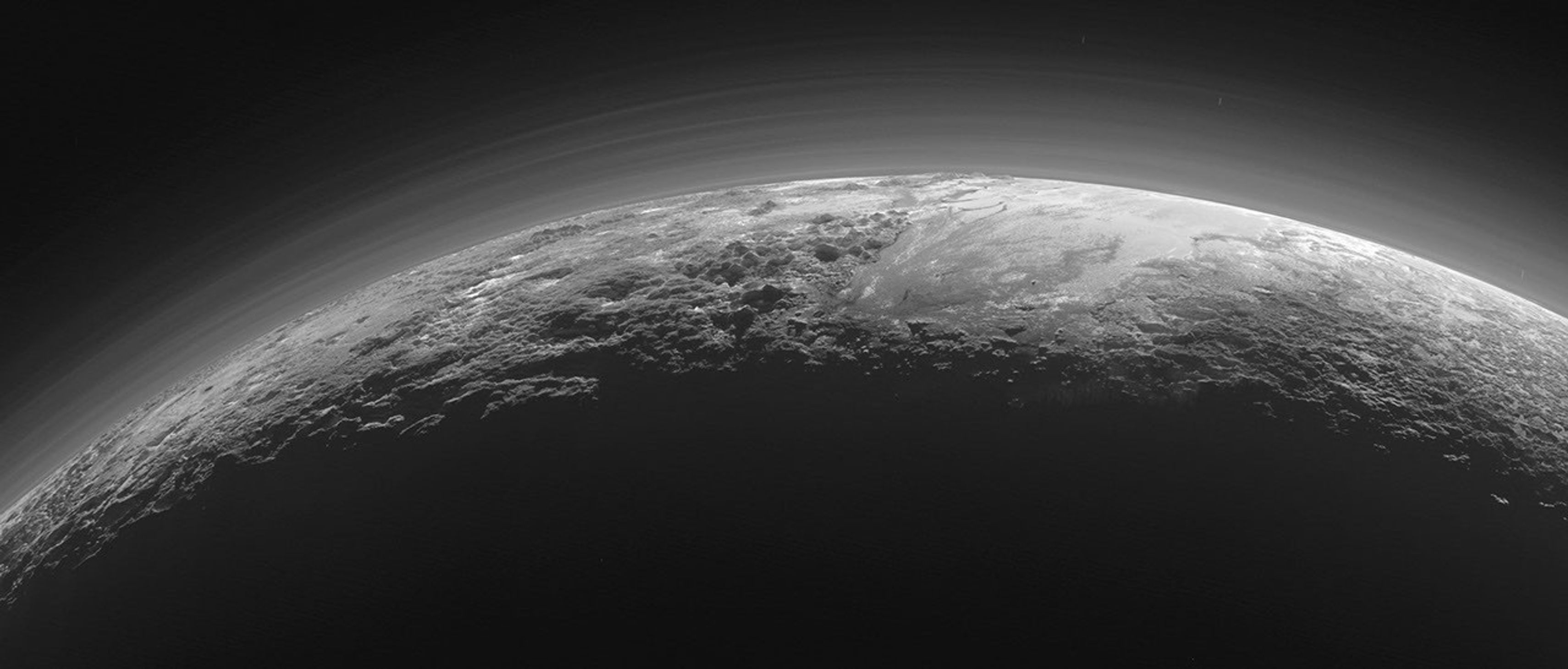 Black-and-white image of Pluto’s rugged surface and hazy atmosphere