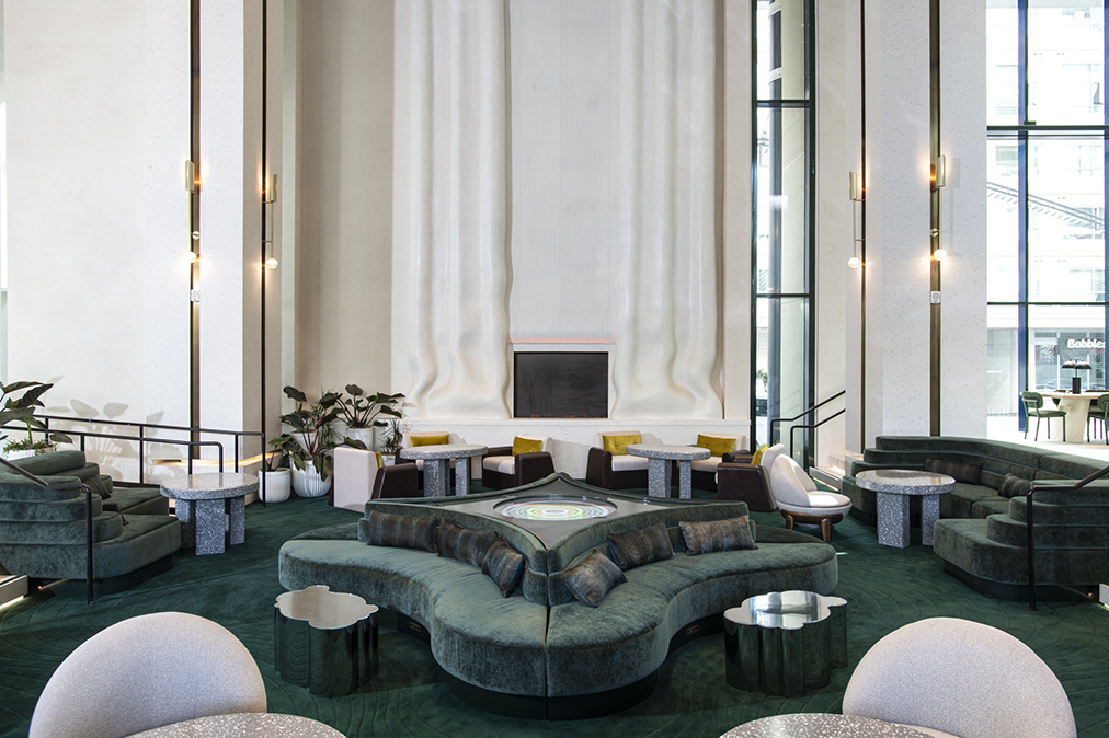 High-ceilinged lounge area with curvy green couches and a wall in the shape of bunched curtains. 