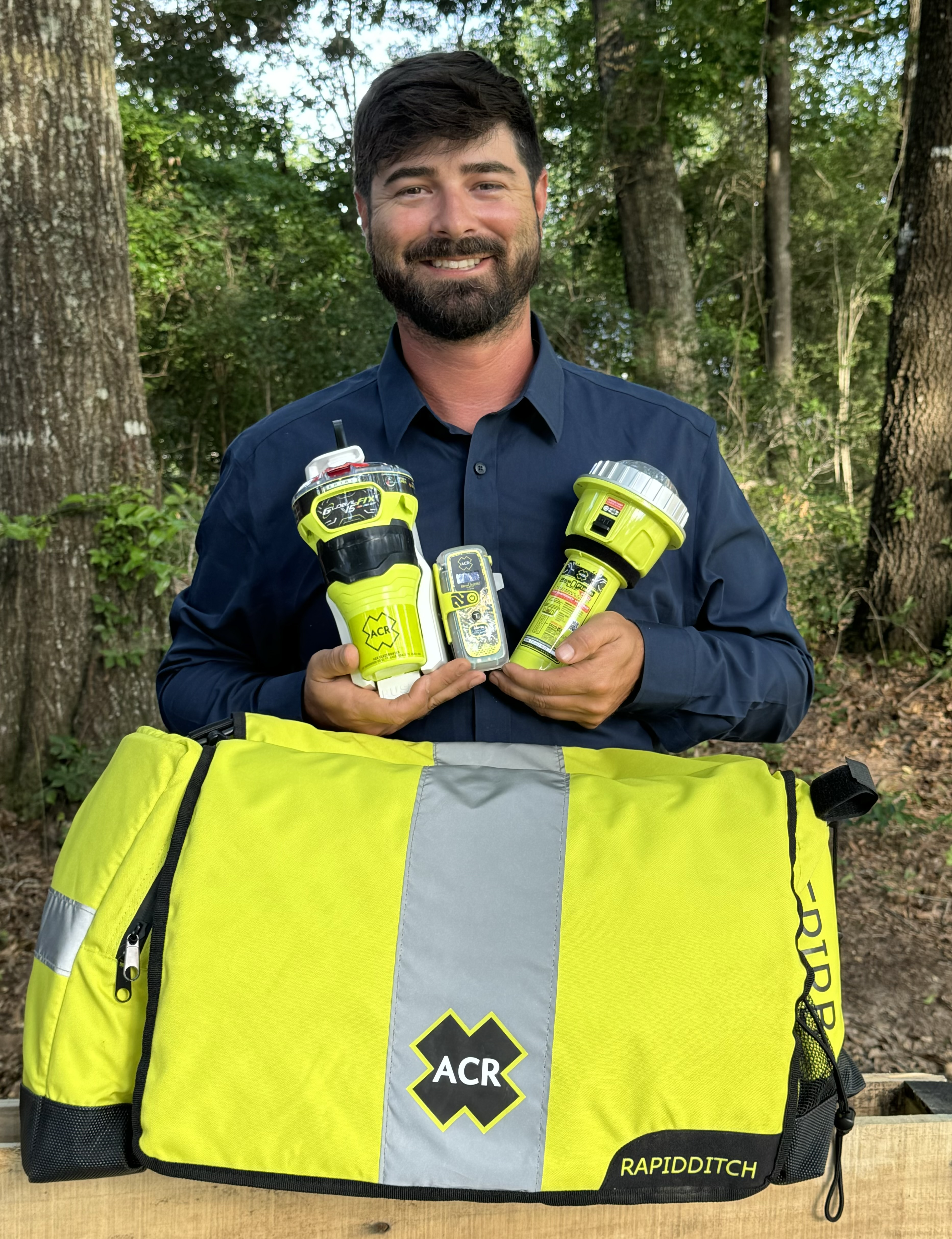 Bearded man holds neon yellow devices next to a same-colored padded bag in a forest setting. 