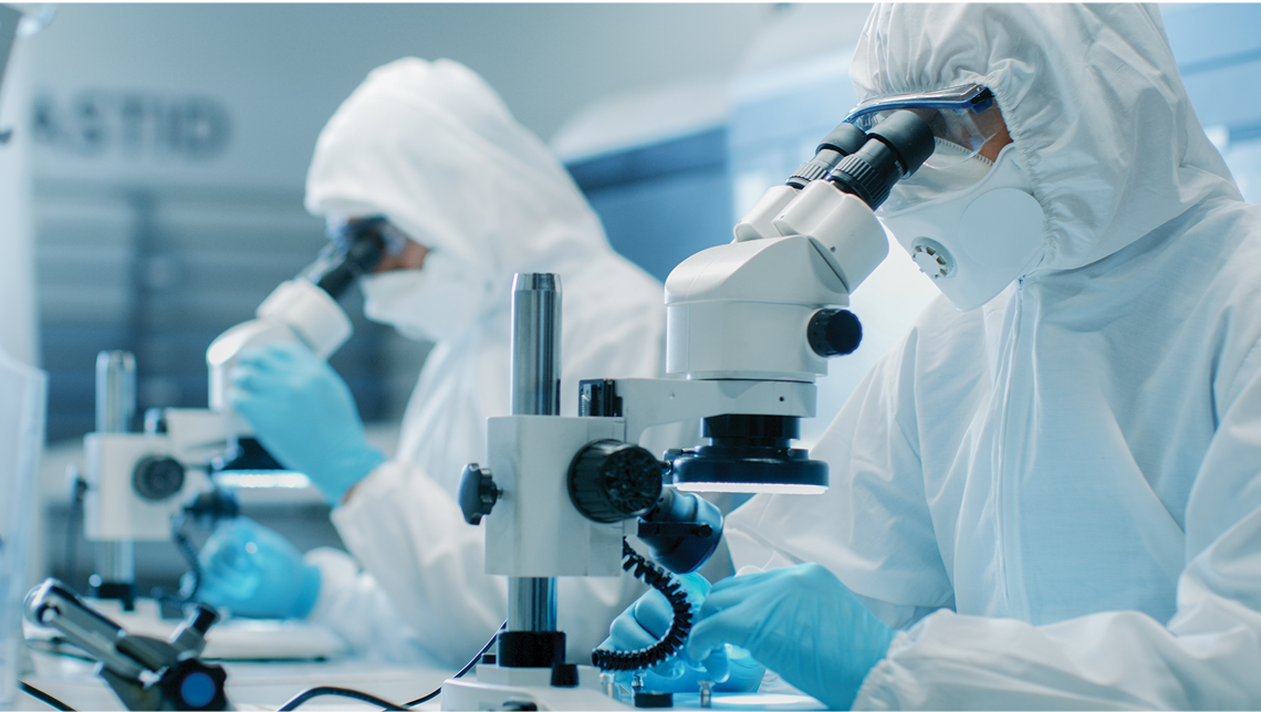 Workers in clean-room suits look through microscopes