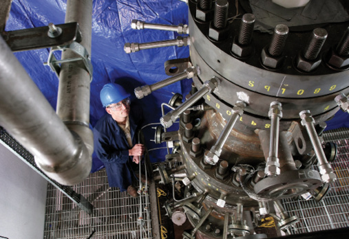 A worker in a blue hard hat looks up at a GTI R-Gas Gassifier