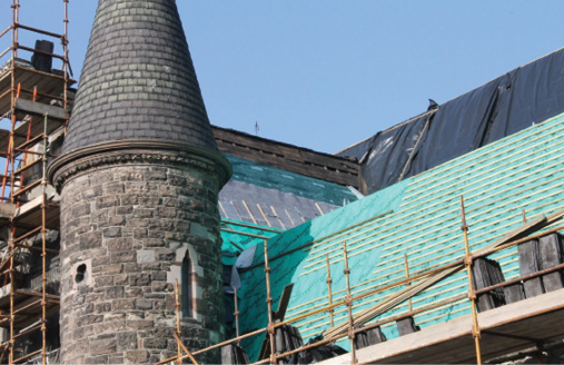 Scaffolding around a stone turret with insulation covering other parts of the historic building