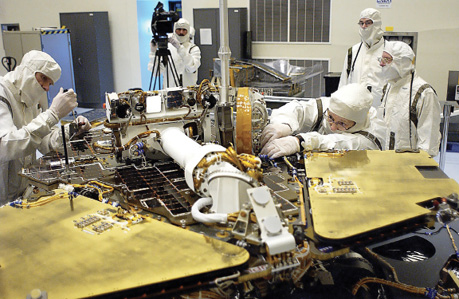Technicians in clean room gear remove a circuit board from the Mars Exploration Rover 2