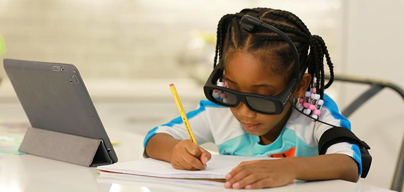 A girl wears Narbis glasses while writing, with a tablet nearby