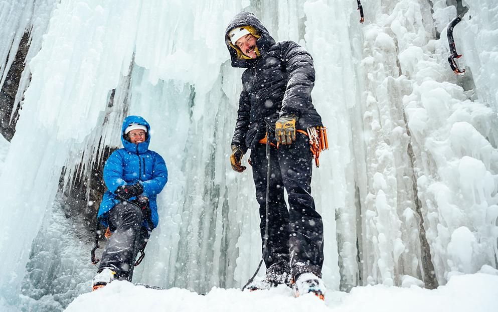 A woman and a man in cold weather gear by a frozen waterfall