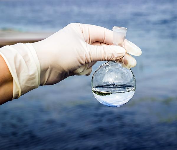 A gloved hand holds a beaker of water