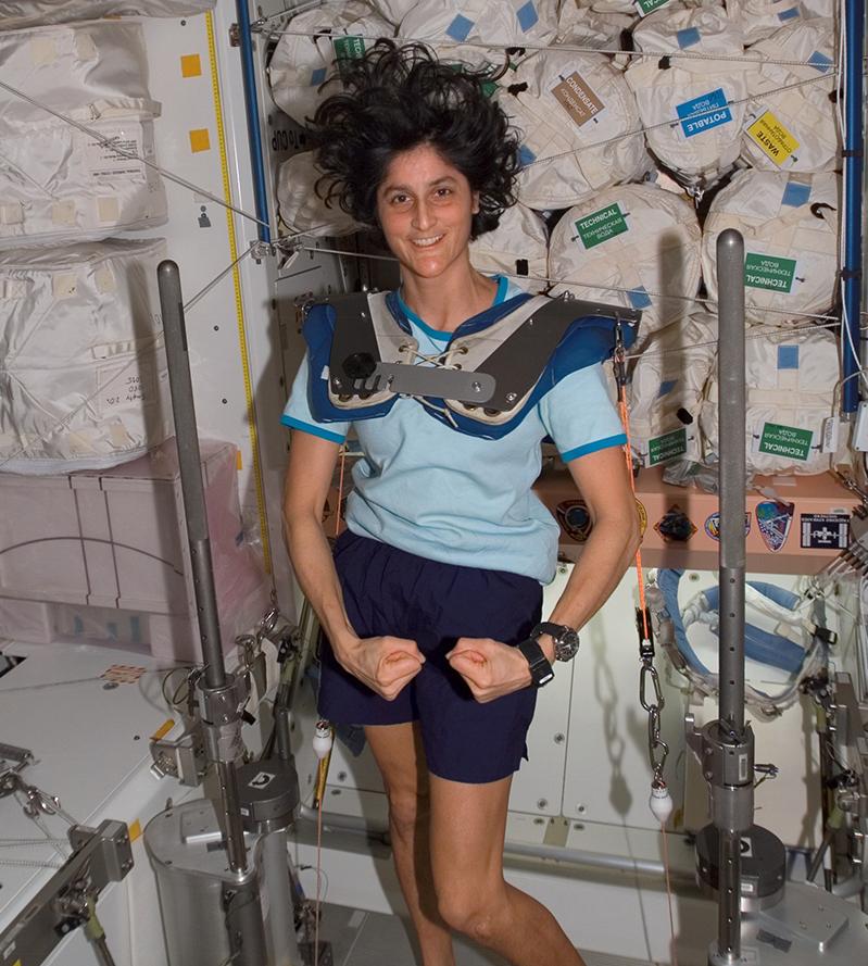 Astronaut Sunita Williams poses while using the Interim Resistive Exercise Device on the ISS. Parts of this device would go on to power the Bowflex Revolution and other commercial exercise equipment. Credit: NASA Astronaut Sunita Williams poses while using the Interim Resistive Exercise Device on the ISS