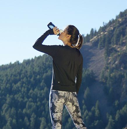 A woman drinks from a water purification bottle on a mountain hike