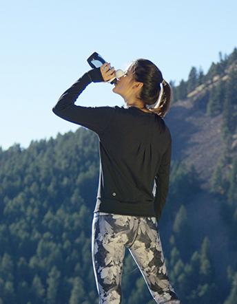 A hiker drinks from a Pod+ water bottle from nkd LIFE