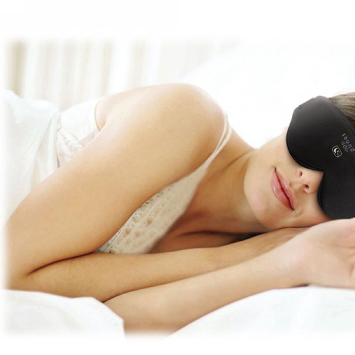 A woman lies in bed wearing the Illumy sleep mask. A smartphone shows the Illumy app interface.