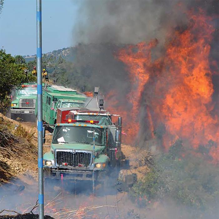 A convoy of firetrucks next to raging forest fire