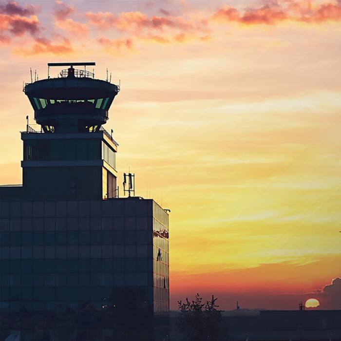 An air traffic control tower with an airliner taking off in the distance